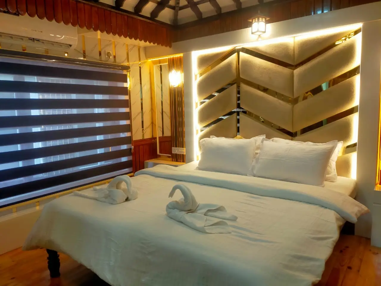 Air-conditioned bedroom with backlit chevron headboard and towel swans on a Kerala houseboat
