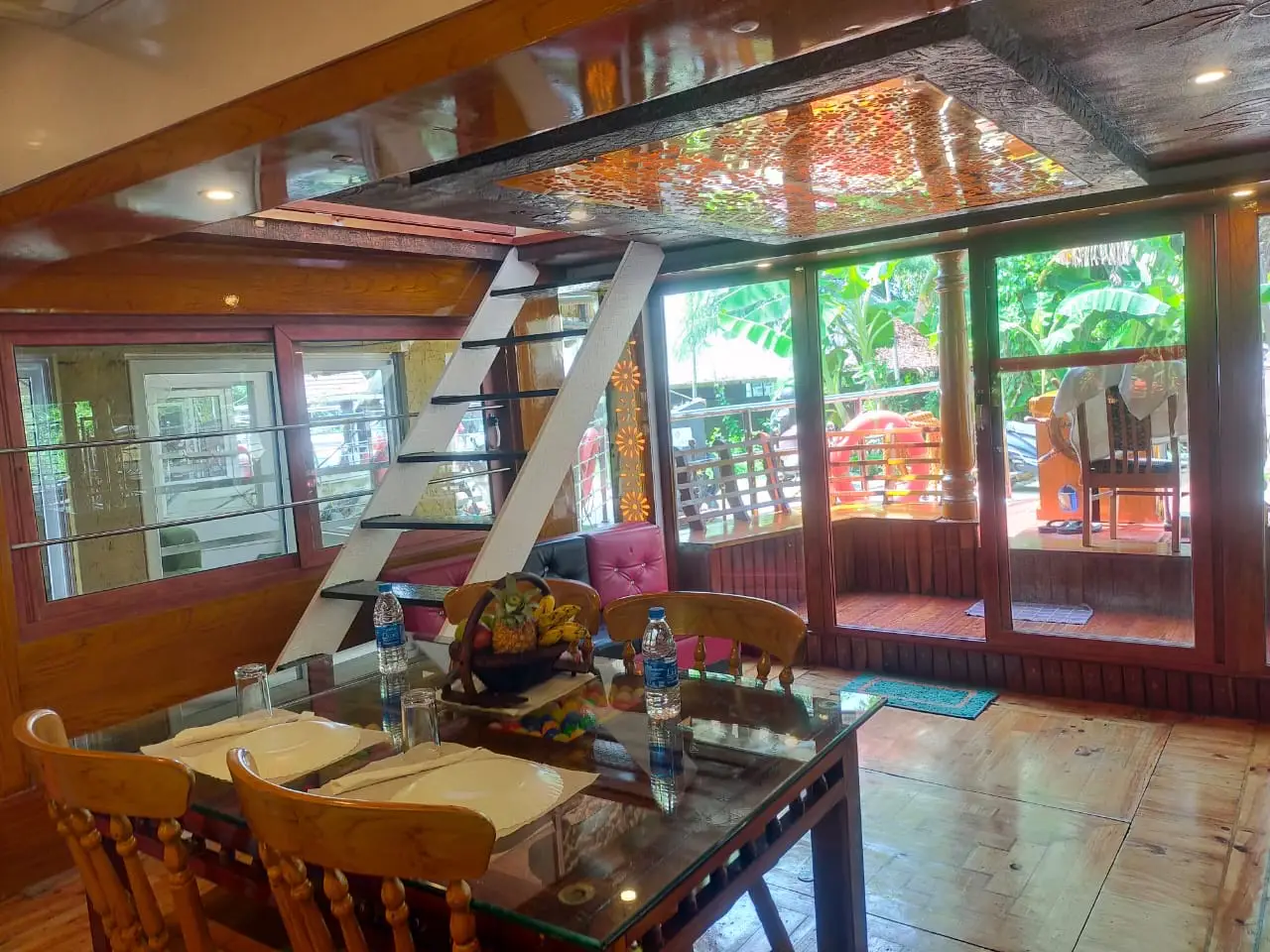 Dining hall with glass-top table and staircase to the upper deck on an Alleppey houseboat