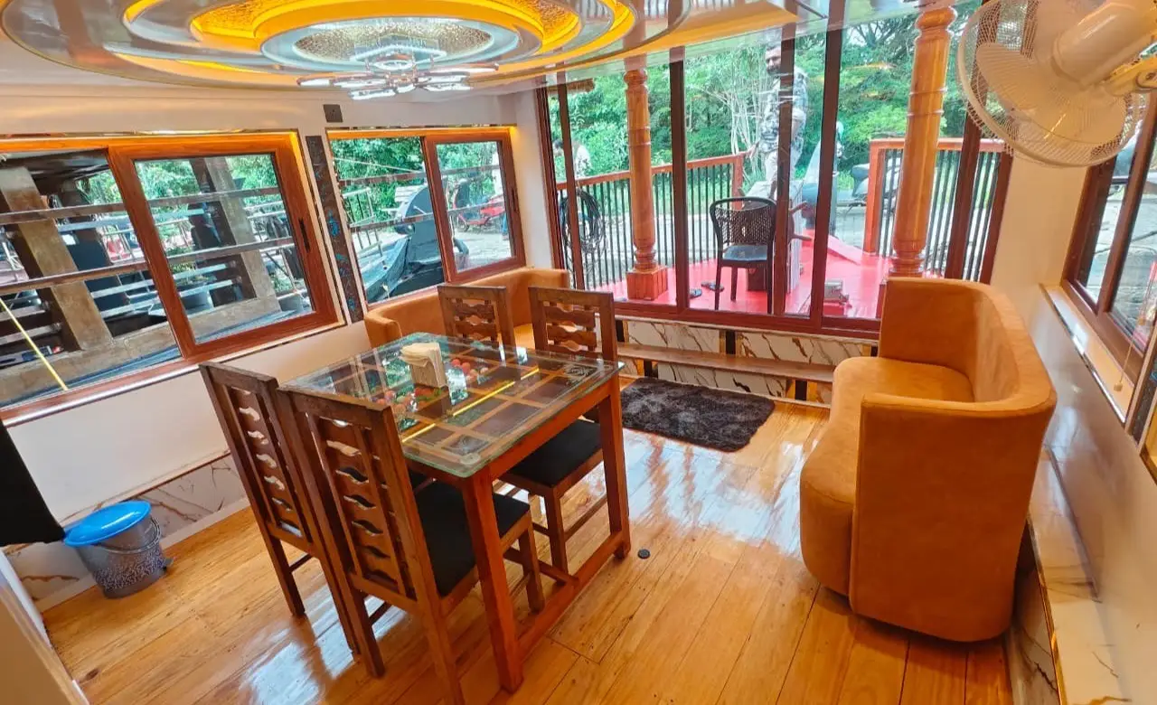 Glass-top dining table and tub chairs in the lounge of a 1-bedroom Alleppey houseboat
