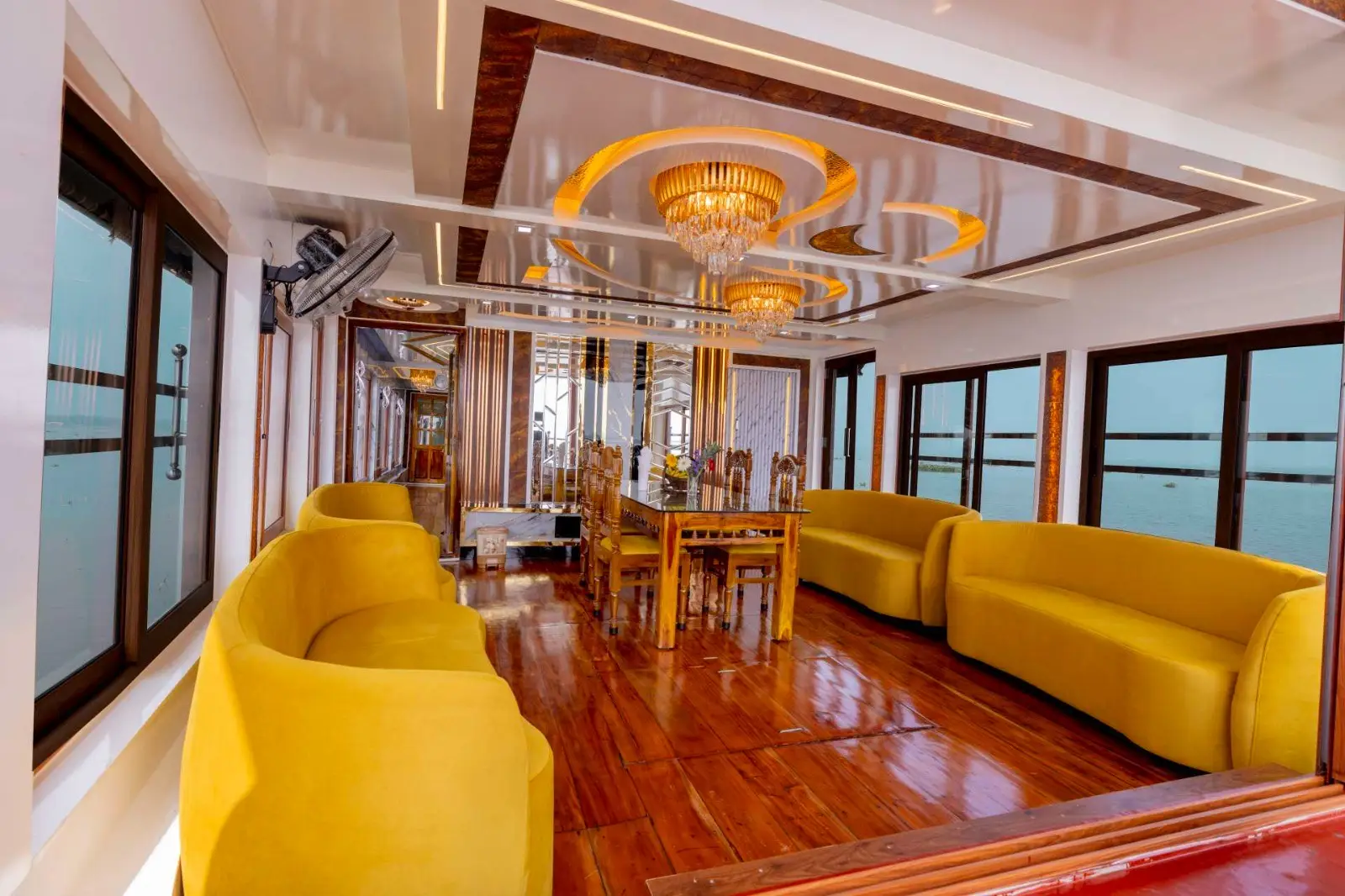 Lounge and dining area with yellow sofas and chandeliers on a premium Alleppey houseboat