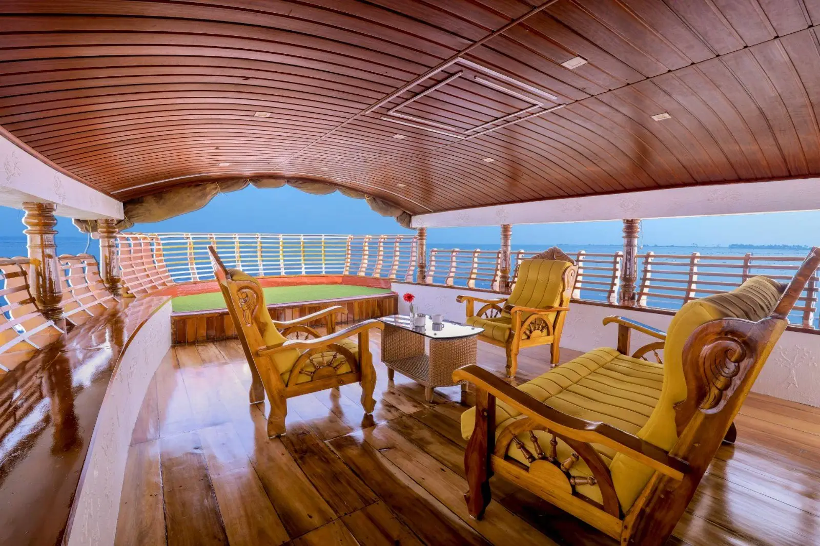 Upper deck lounge with cane armchairs overlooking Vembanad lake at sunset