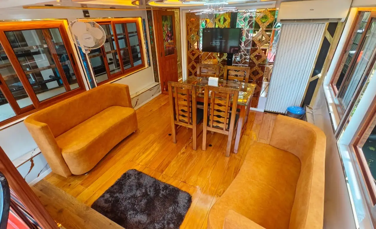 Upper deck lounge with sofas, dining table and television on a premium Kerala houseboat