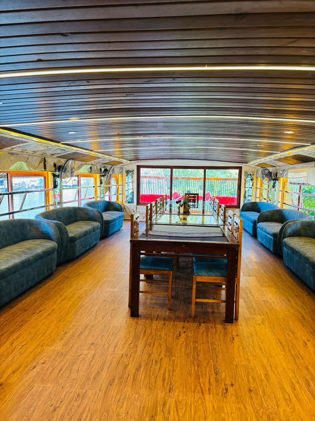 Upper deck lounge with sofa seating and long dining table on a Kerala houseboat